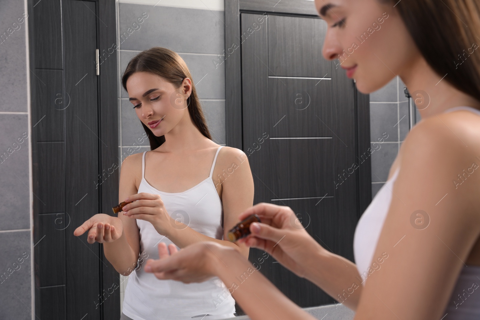 Photo of Young woman applying essential oil onto wrist in bathroom