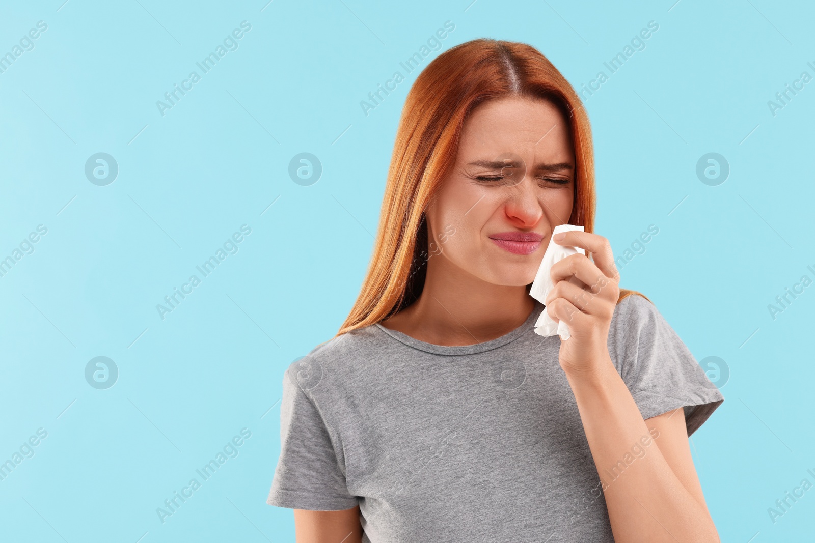 Photo of Suffering from allergy. Young woman with tissue sneezing on light blue background, space for text
