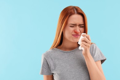 Suffering from allergy. Young woman with tissue sneezing on light blue background, space for text