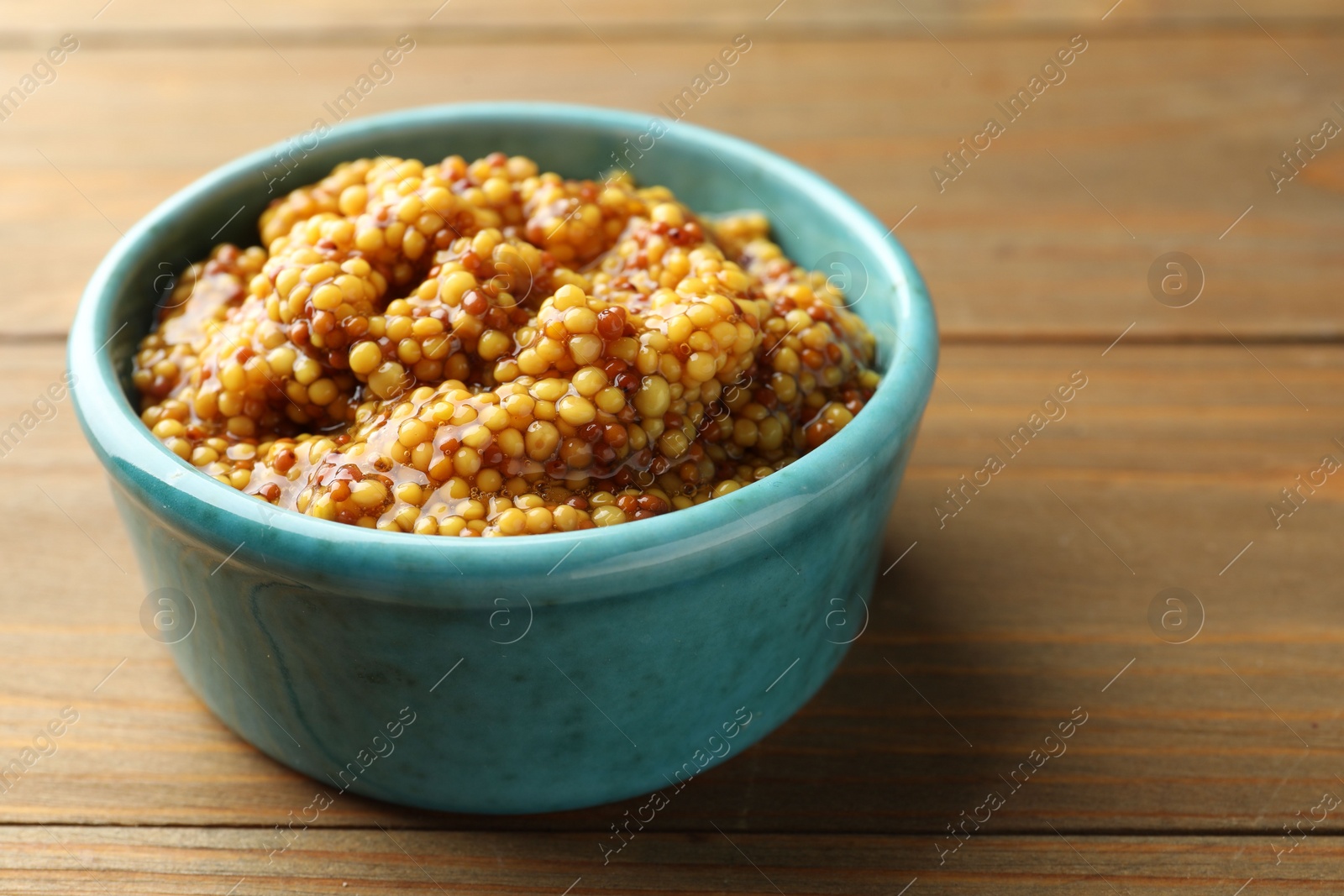 Photo of Fresh whole grain mustard in bowl on wooden table, closeup. Space for text