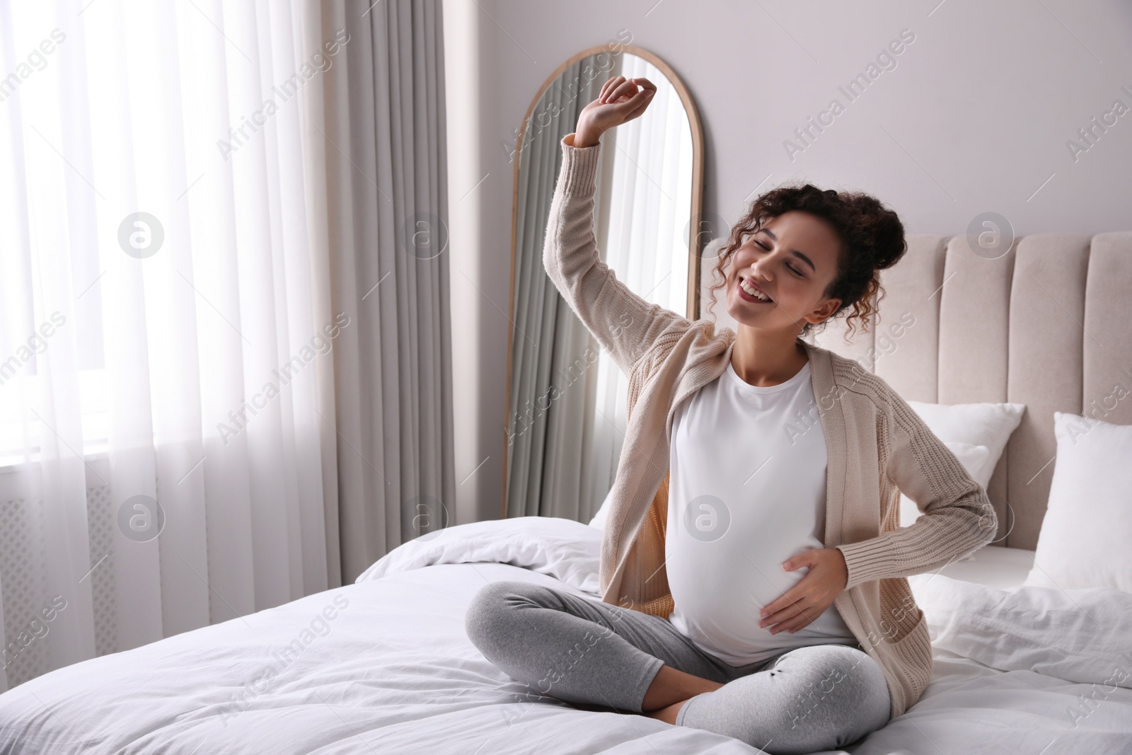 Photo of Excited pregnant young African-American woman sitting on bed at home