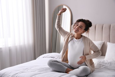 Photo of Excited pregnant young African-American woman sitting on bed at home