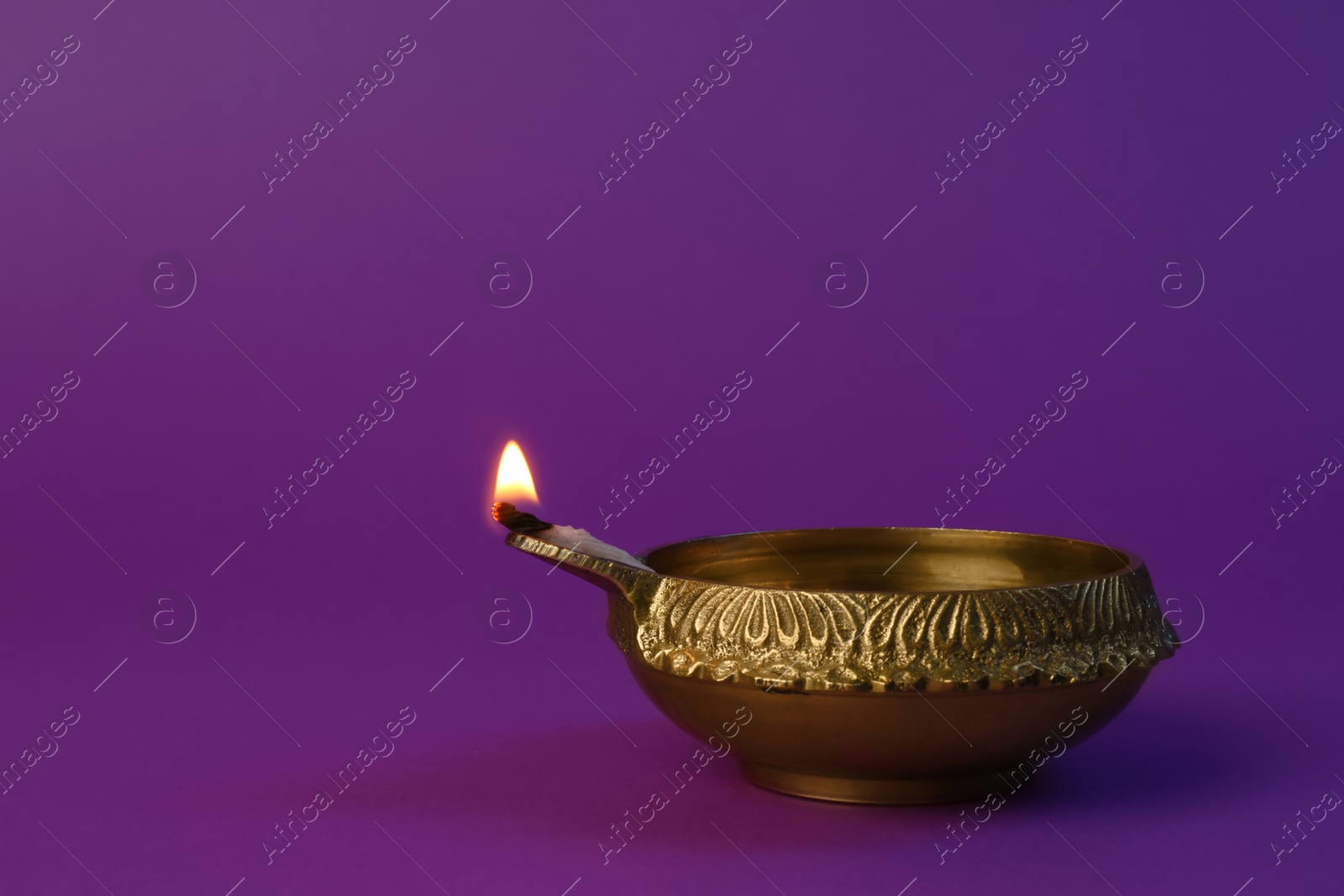 Photo of Lit diya lamp on purple background, space for text. Diwali celebration