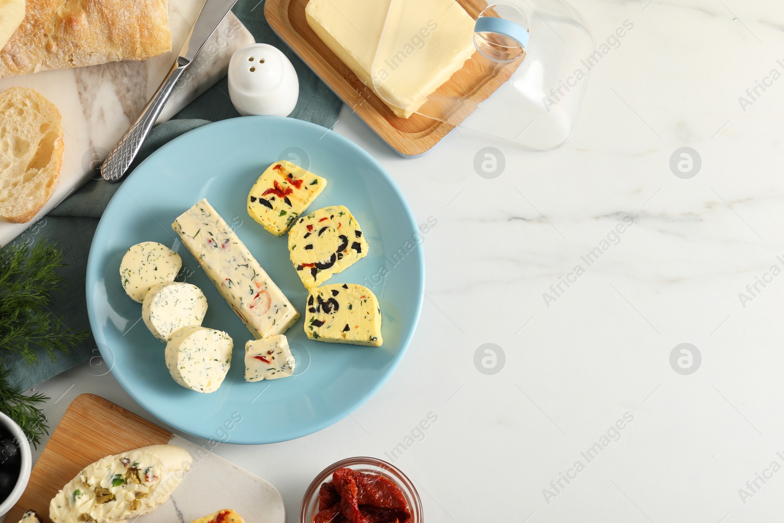 Photo of Different types of tasty butter, dill, chili and bread on white marble table, top view. Space for text