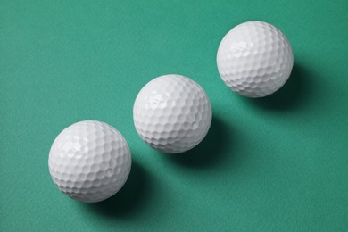 Three golf balls on green background, flat lay