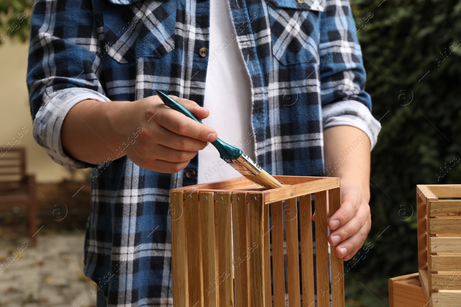 Photo of Man applying varnish onto wooden crate at table outdoors, closeup