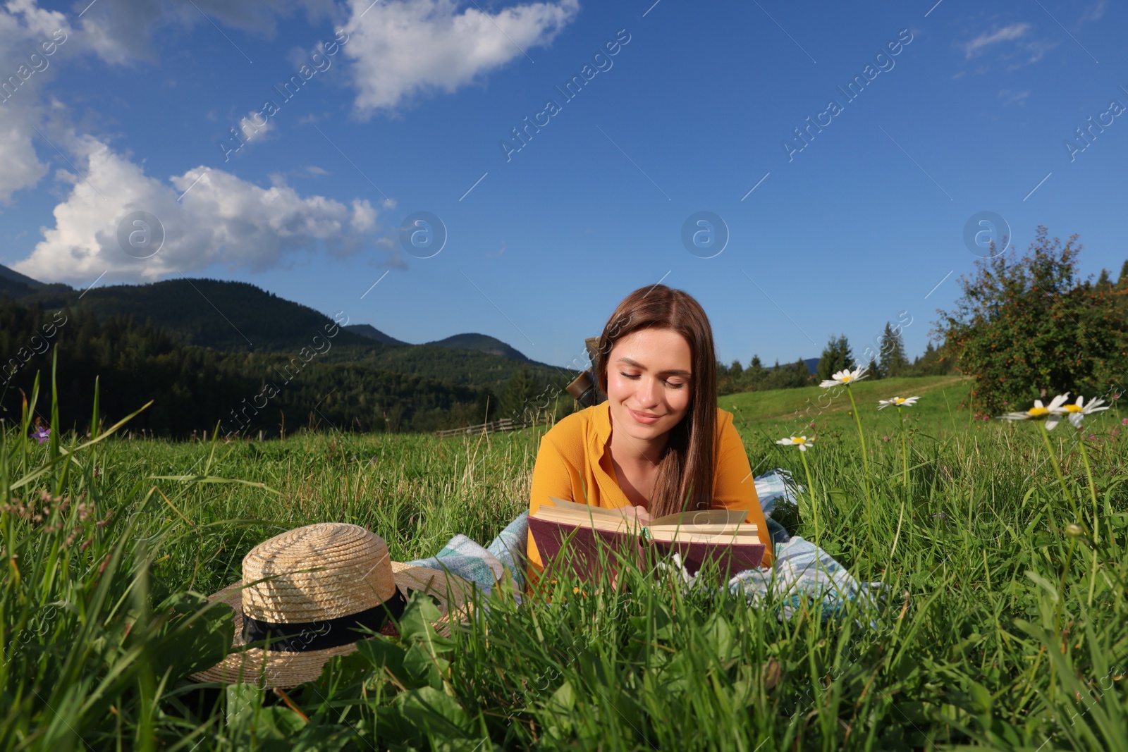 Photo of Beautiful young woman reading book on green meadow in mountains