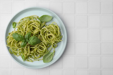 Photo of Delicious pasta with pesto sauce and basil on white tiled table, top view. Space for text