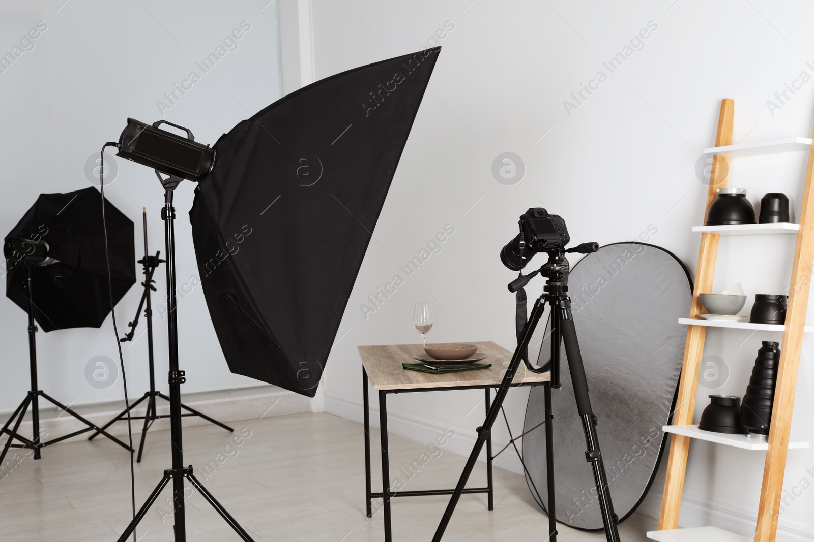 Photo of Table with stylish dinnerware in front of camera and professional lighting equipment indoors. Photo studio set