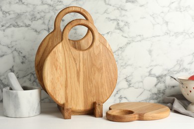 Photo of Wooden cutting boards and mortar with pestle on white table near marble wall
