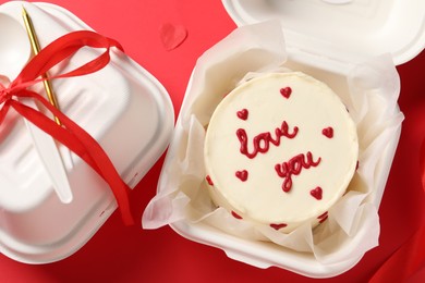 Photo of Bento cake with Love You text in box and takeaway packaging on red table, top view. St. Valentine's day surprise