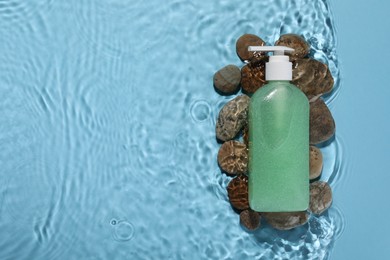 Bottle of face cleansing product and stones in water against light blue background, flat lay. Space for text