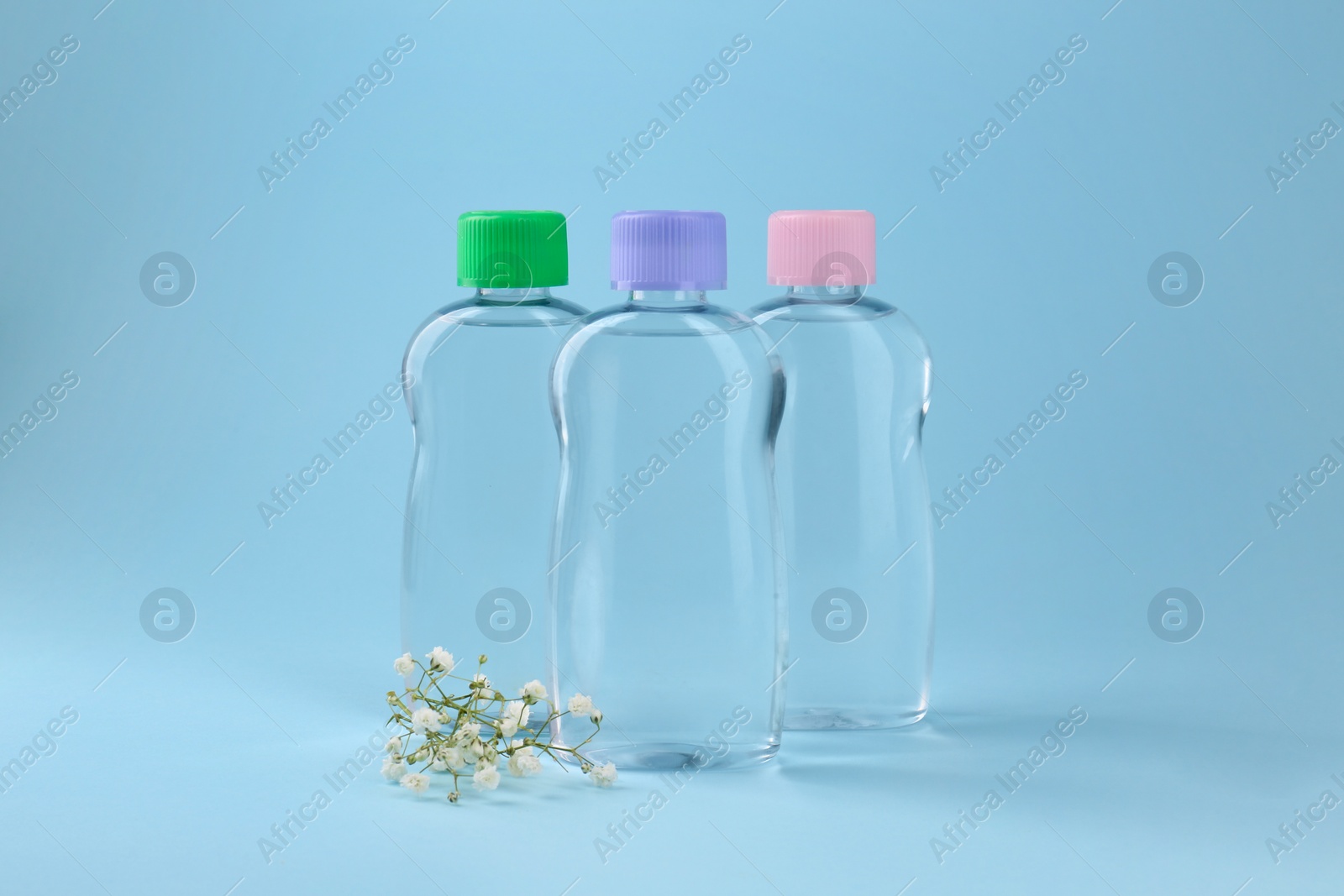 Photo of Bottles with baby oil and gypsophila on light blue background. Space for text