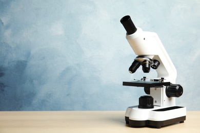 Photo of Modern microscope on wooden table against blue background, space for text. Medical equipment