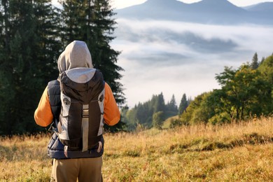 Tourist with backpack in mountains on sunny day, back view. Space for text