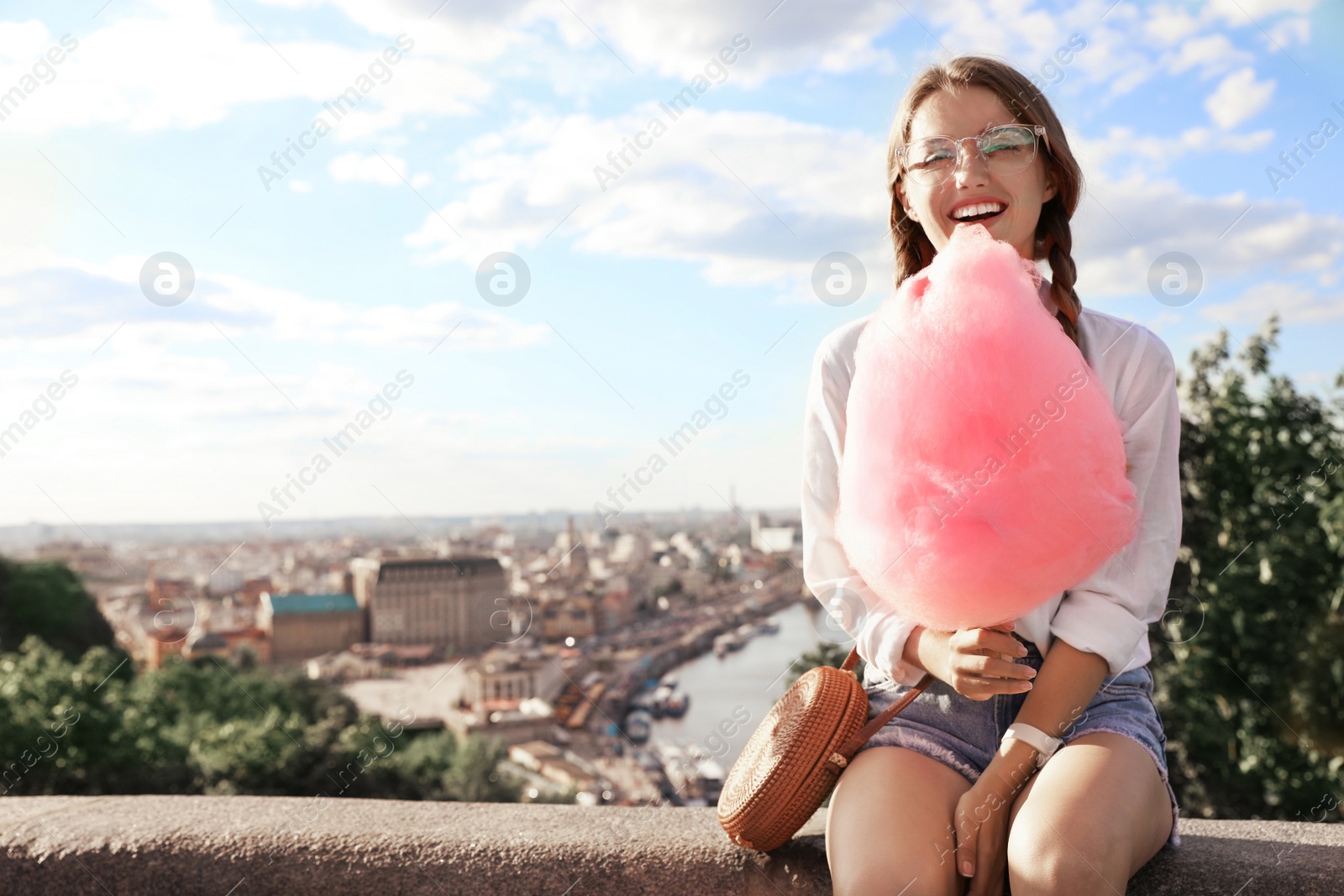 Photo of Young woman with cotton candy outdoors on sunny day. Space for text