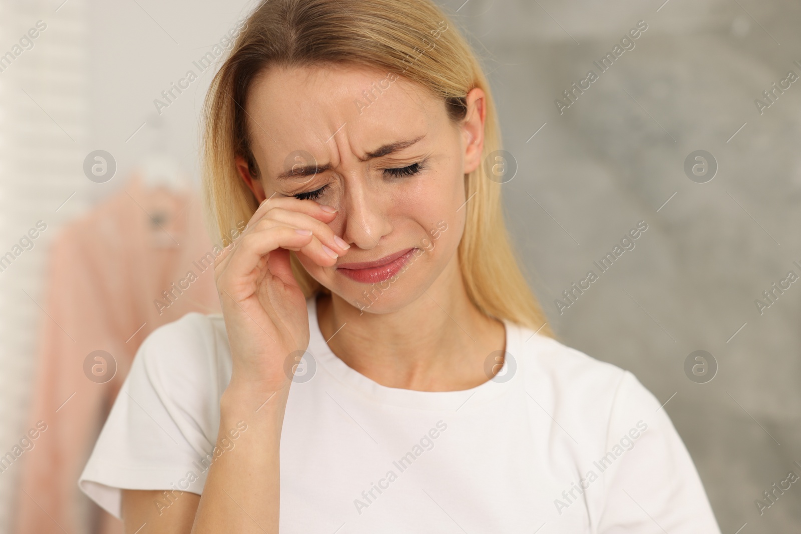 Photo of Sad woman with smeared mascara crying indoors