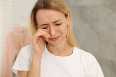 Sad woman with smeared mascara crying indoors