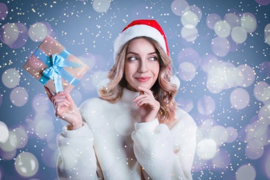 Beautiful young woman in Santa hat with Christmas present on color background