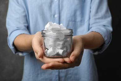 Woman holding glass jar with paper pieces, closeup on hands