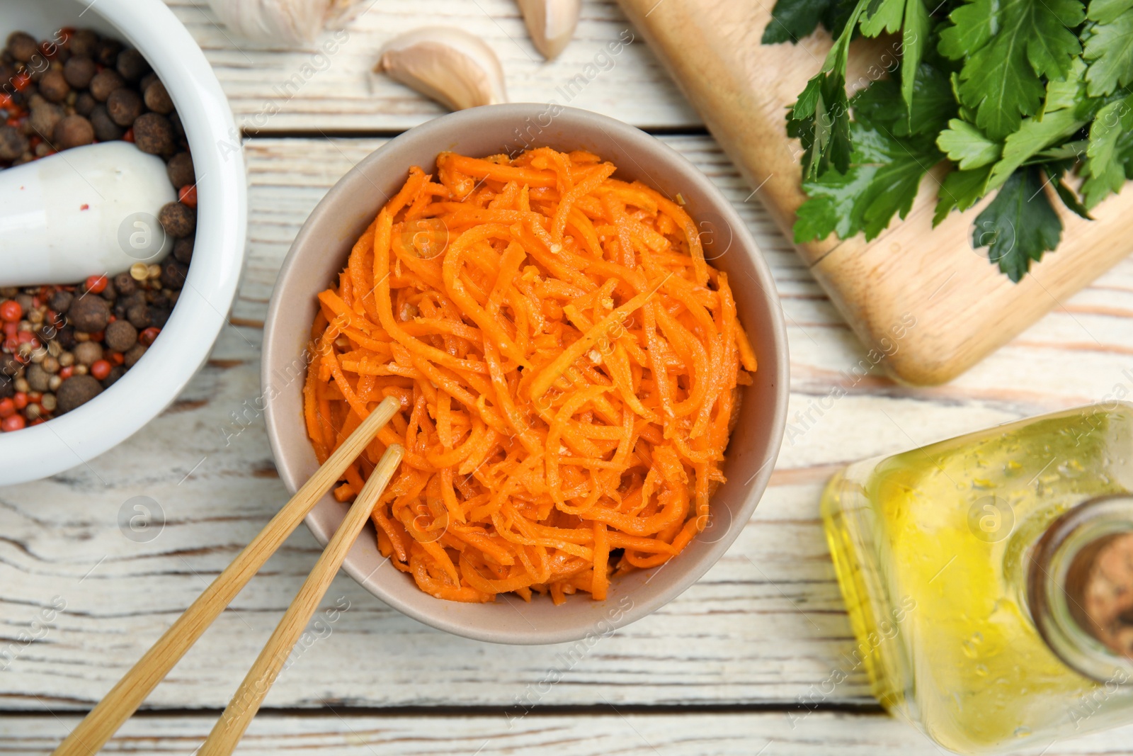 Photo of Delicious Korean carrot salad, oil, spices and parsley on white wooden table, flat lay