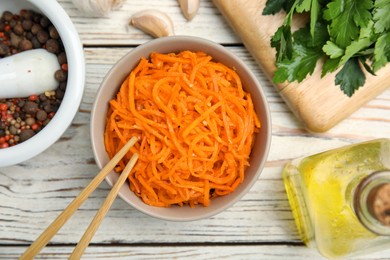 Photo of Delicious Korean carrot salad, oil, spices and parsley on white wooden table, flat lay