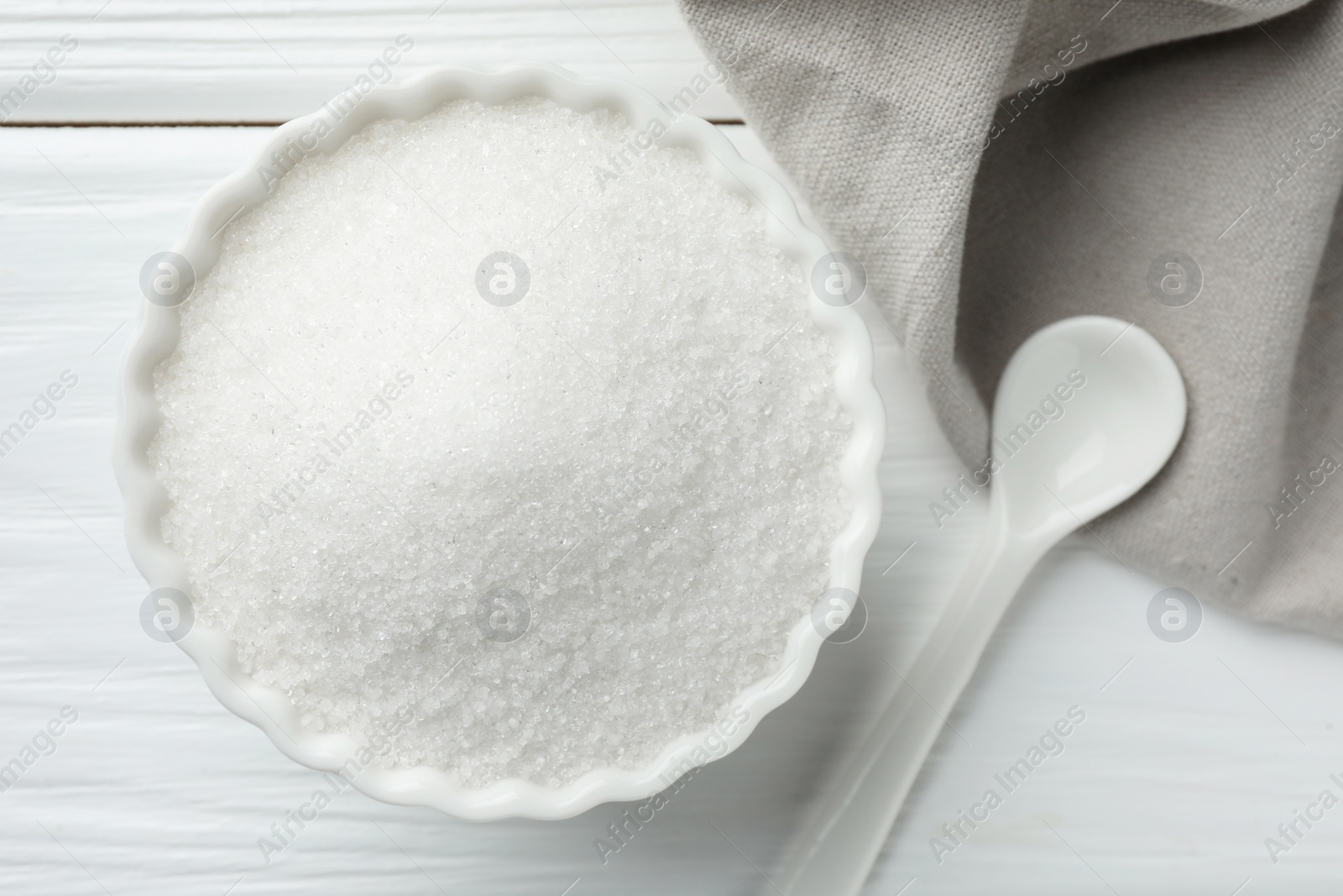 Photo of Granulated sugar in bowl and spoon on white wooden table, top view