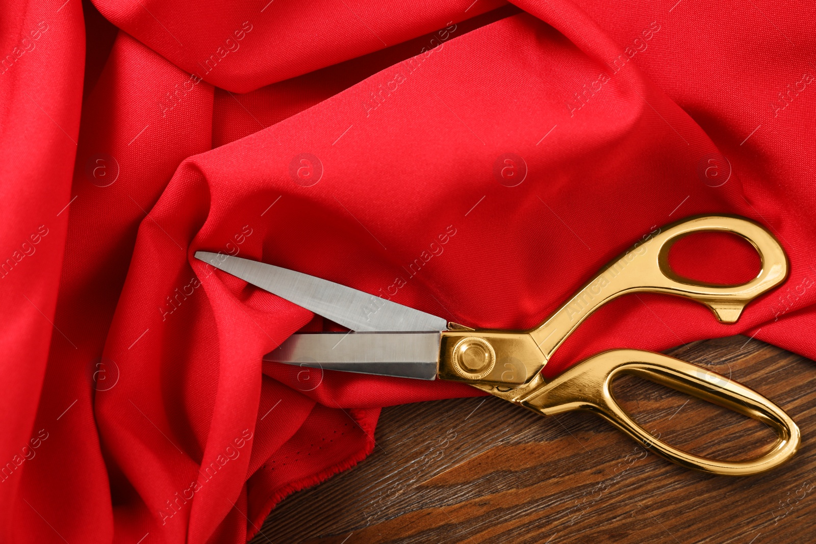 Photo of Red fabric and sharp scissors on wooden table, flat lay