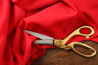 Red fabric and sharp scissors on wooden table, flat lay