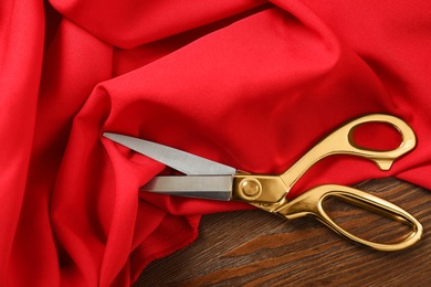 Photo of Red fabric and sharp scissors on wooden table, flat lay