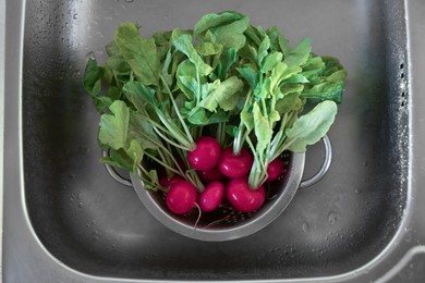 Fresh wet radishes in metal colander inside sink, top view