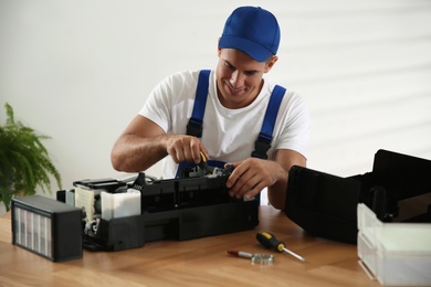 Repairman with screwdriver fixing modern printer in office