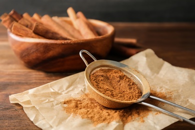 Sieve with aromatic cinnamon powder on wooden table