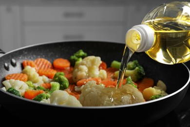 Photo of Pouring cooking oil from bottle into frying pan with vegetables, closeup