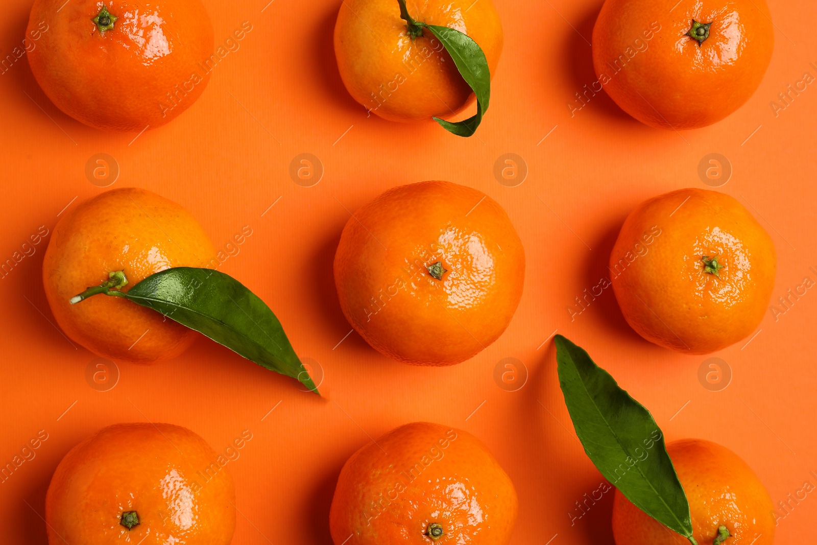 Photo of Delicious tangerines with green leaves on orange background, flat lay