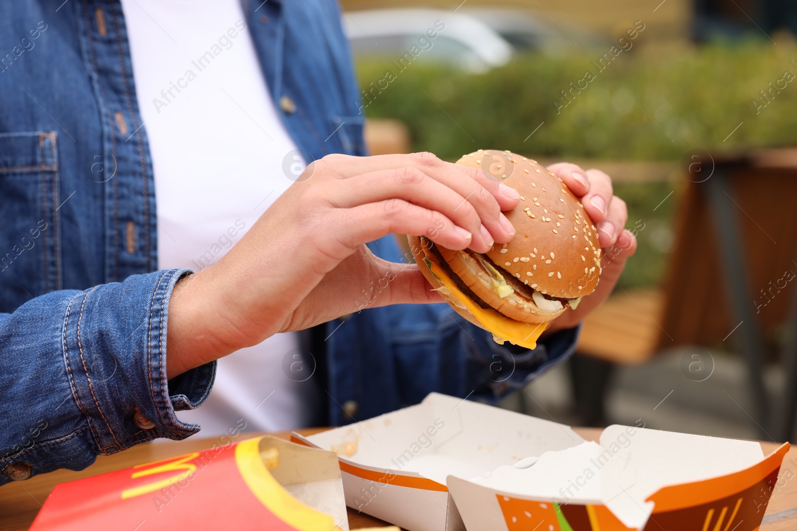 Photo of Lviv, Ukraine - October 9, 2023: Woman with McDonald's burger at table outdoors, closeup