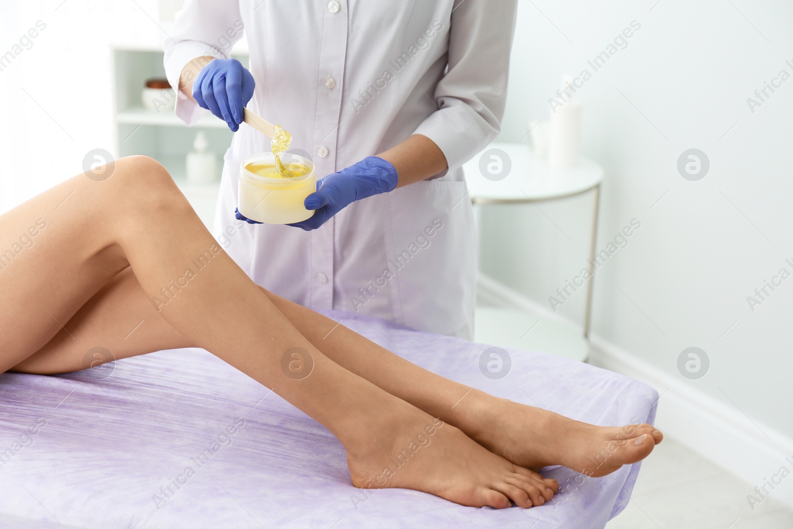 Photo of Woman getting wax epilation of legs in salon, closeup