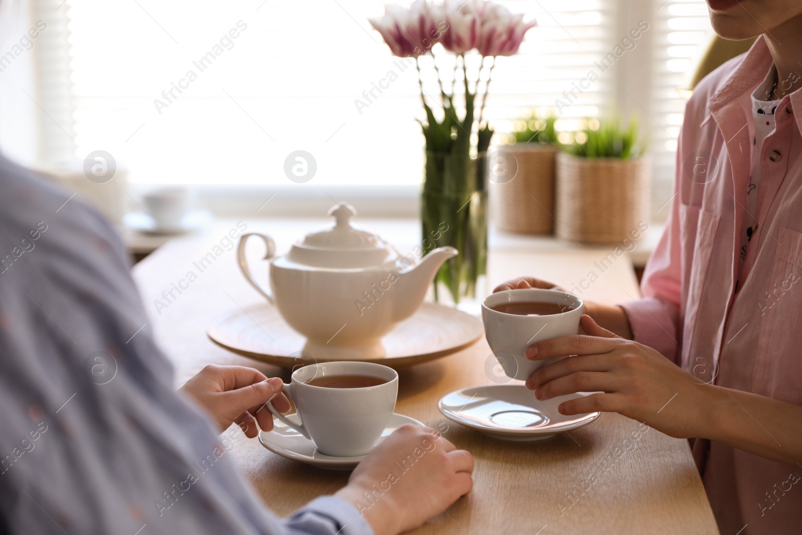 Photo of Women with cups of tea at table near window indoors, closeup