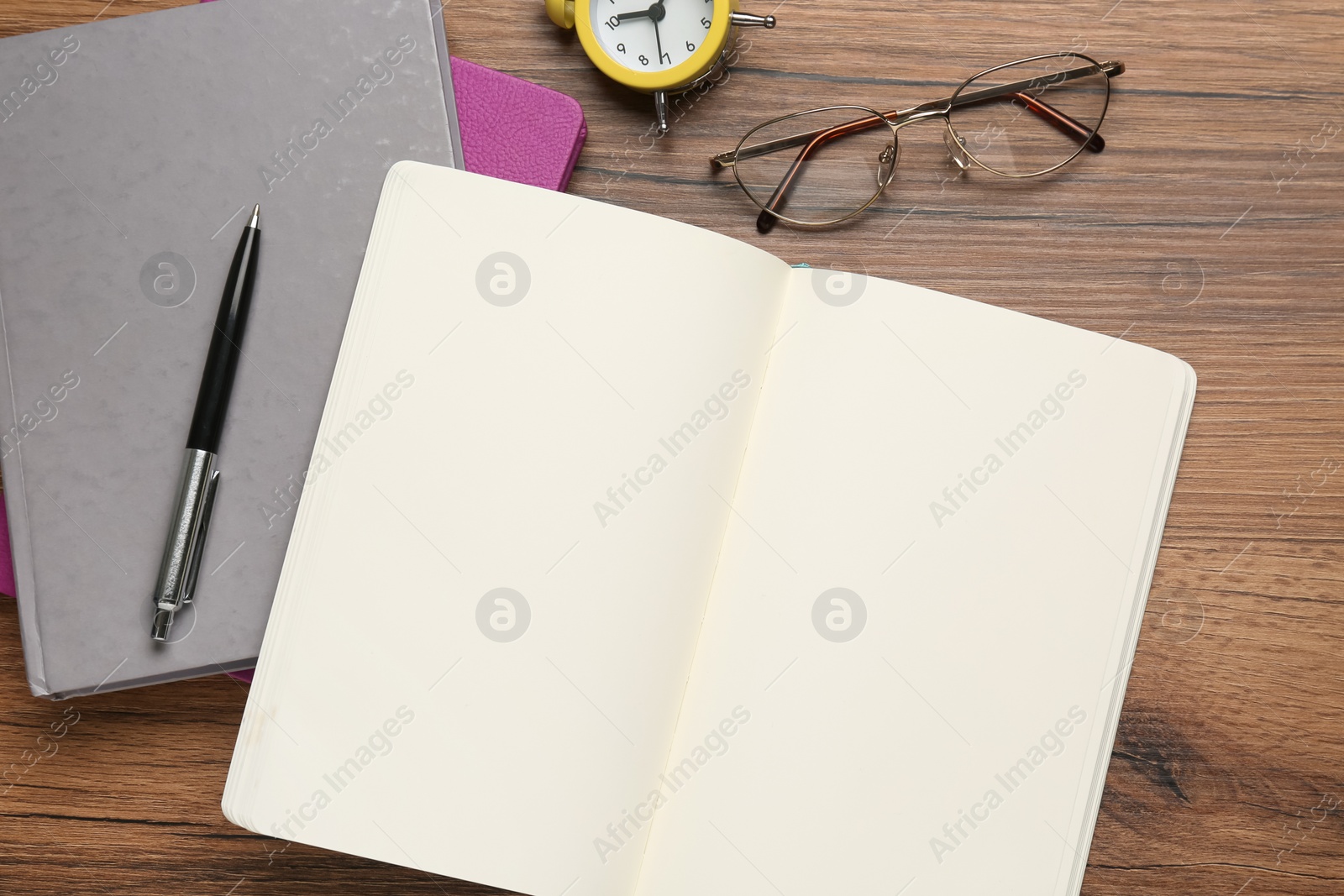 Photo of Notebooks, pen, glasses and alarm clock on wooden table, flat lay. Space for text