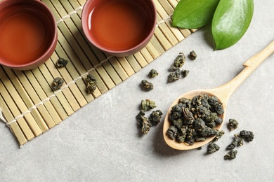 Composition with spoon of Tie Guan Yin Oolong tea and brewed beverage on grey table, top view