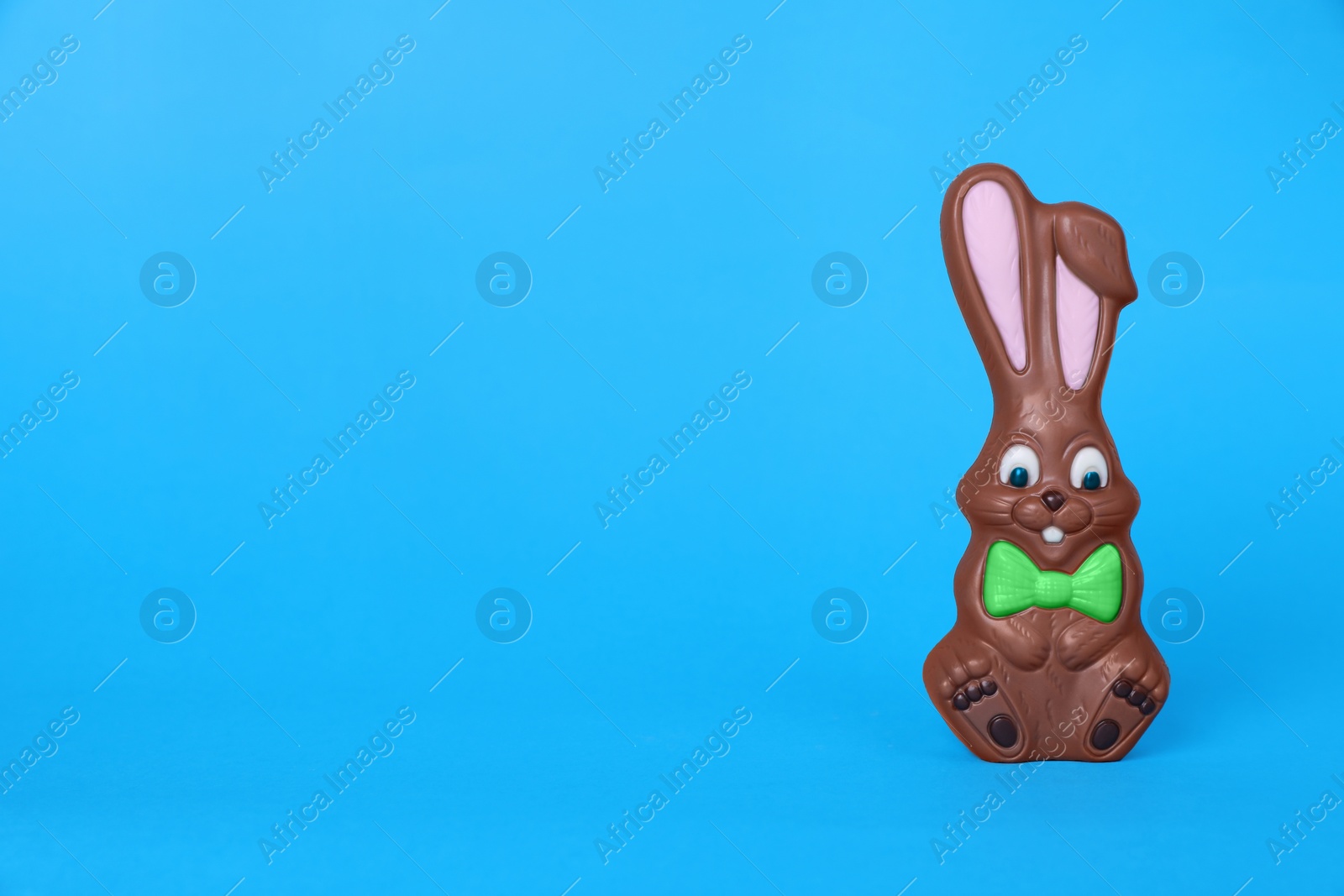 Photo of Chocolate bunny on light blue background, space for text. Easter celebration