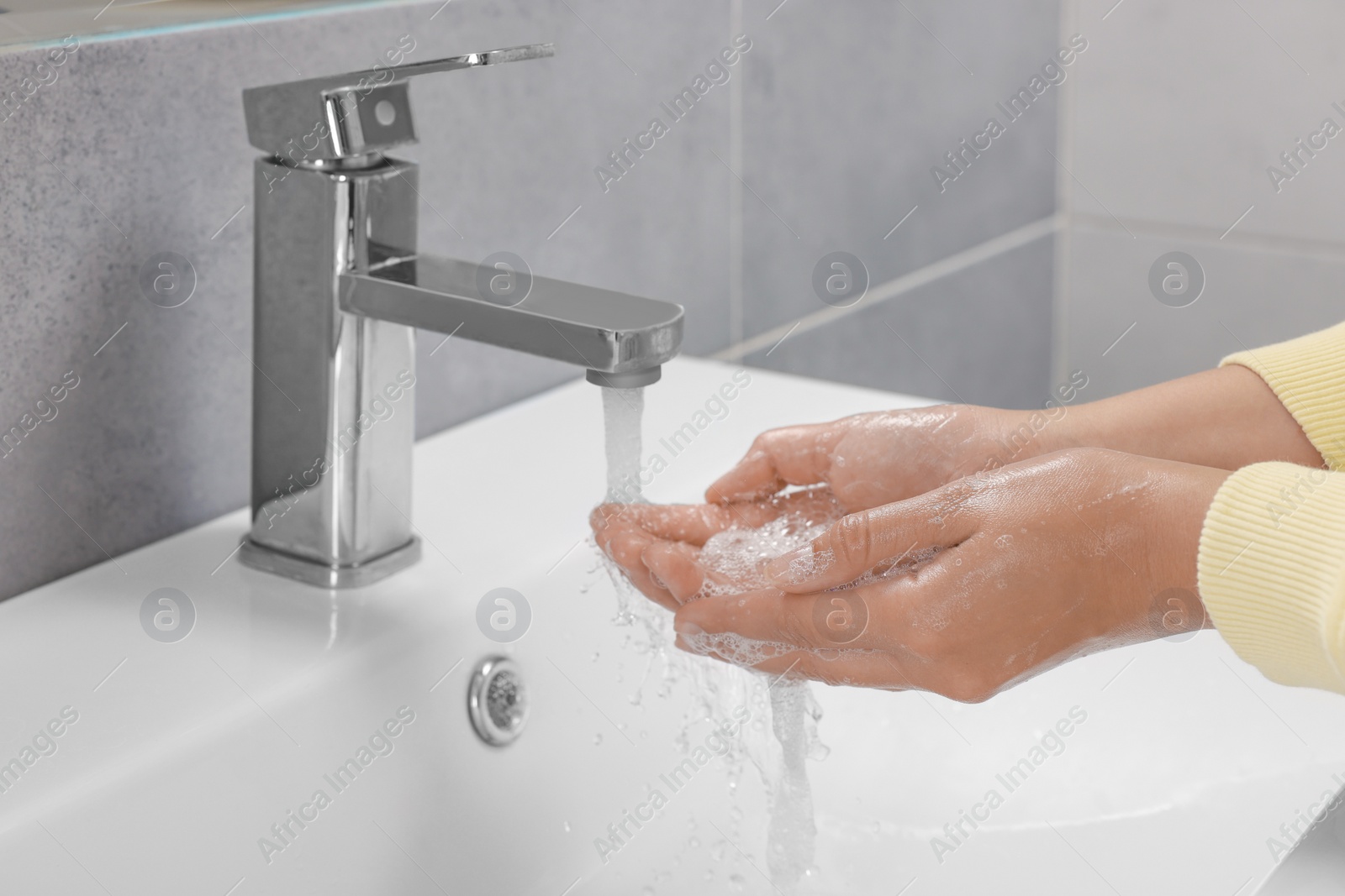 Photo of Woman washing hands with water from tap in bathroom, closeup