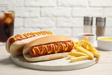 Photo of Delicious hot dogs with mustard, ketchup and potato fries on white wooden table, closeup