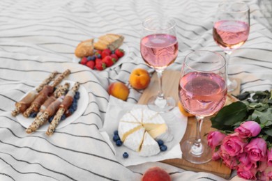 Photo of Glasses of delicious rose wine, flowers and food on white picnic blanket