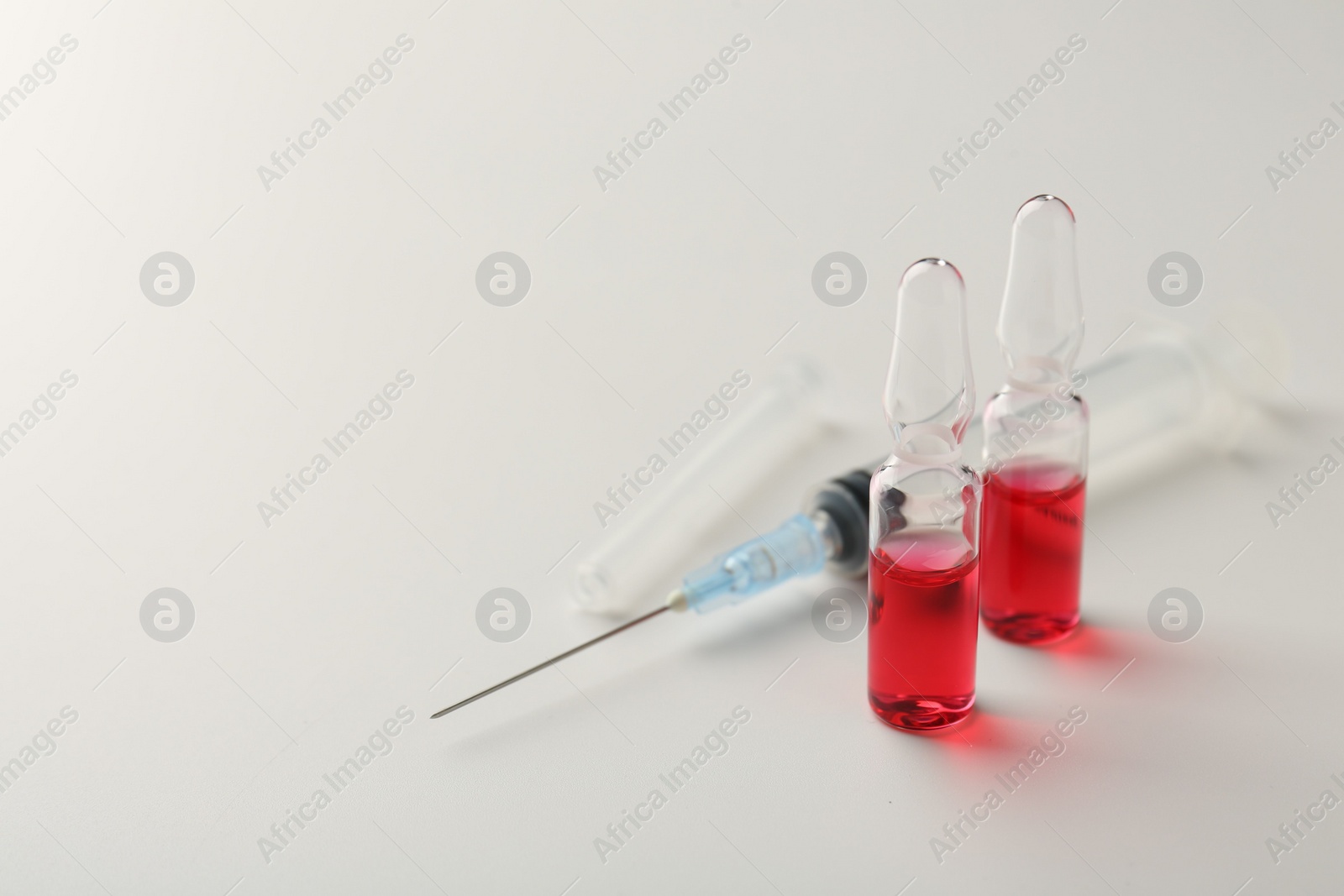 Photo of Glass ampoules with liquid and syringe on white background, closeup. Space for text