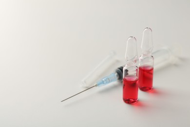 Photo of Glass ampoules with liquid and syringe on white background, closeup. Space for text