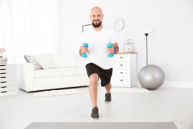 Photo of Overweight man doing exercise with dumbbells at home