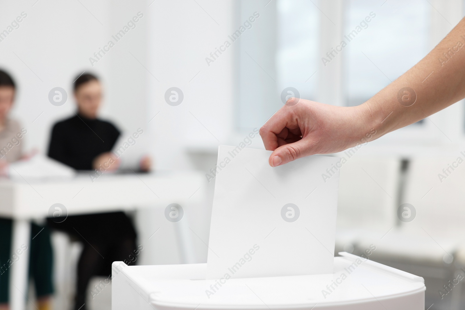 Photo of Woman putting her vote into ballot box on blurred background, closeup