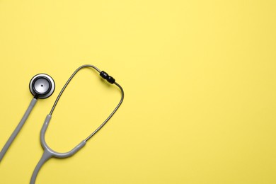 Stethoscope on yellow background, top view. Space for text