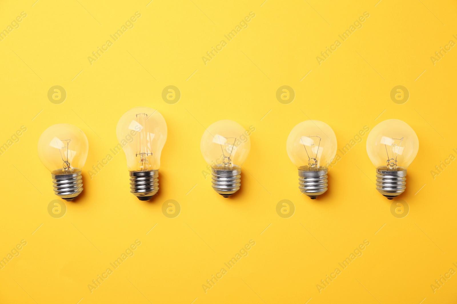 Photo of Vintage and modern incandescent lamp bulbs on yellow background, flat lay